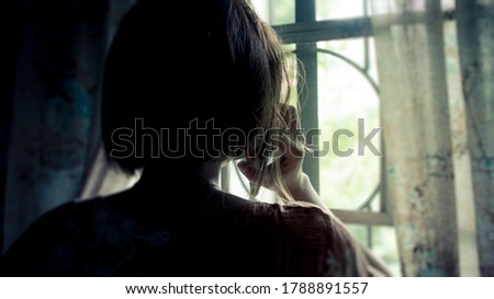 Silhouette of a woman receiving a grim call while facing the window at home. Distress, loss, or sadness concept.