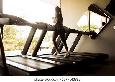 silhouette of woman running on treadmill machine.  sportswoman practicing cardio in gym room with outdoor background
