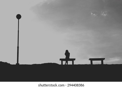 The Silhouette Of Woman Sitting Alone With Grey Sky, Concept Of Lonely, Sad, Alone, Person Space / Single Woman On Valentine