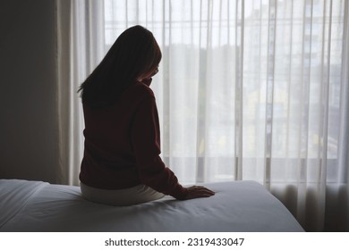 Silhouette of a woman sitting and crying on a bed in bedroom - Powered by Shutterstock