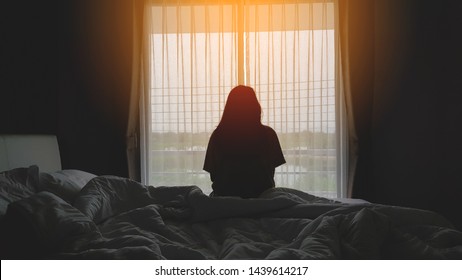 silhouette of woman sitting on the bed beside the windows with sunlight in the morning - Shutterstock ID 1439614217