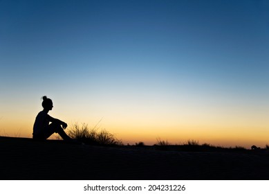 Silhouette Of A Woman Sitting In The Sunset