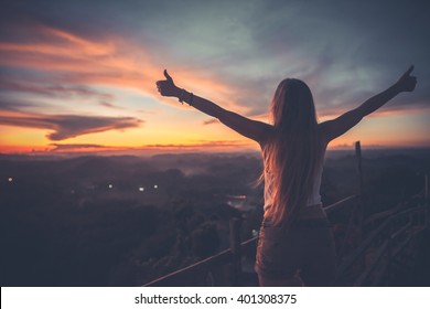 Silhouette Of The Woman Spreading Arms With Her Thumbs Up, Standing High On The Viewpoint With Breathtaking View Over Fields In Sunset Light.Chocolate Hills, Bohol Island, Philippines.