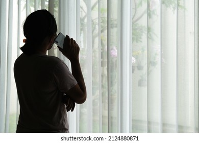 Silhouette of a woman standing by the window making a phone call. - Powered by Shutterstock