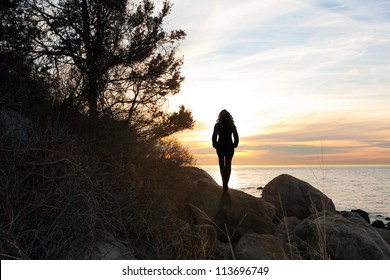 Silhouette of a woman standing in front of the sunset at the New England shoreline.