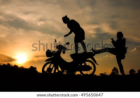Silhouette of the woman standing on the motorcycles, another tease each other on the ground, couple in sunset