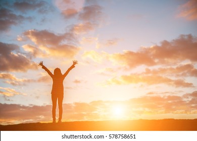 Silhouette Woman At Sunset Standing Elated With Arms Raised Up Above Her Head.