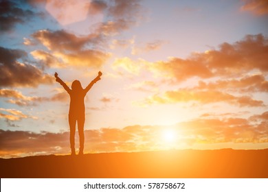 Silhouette Woman At Sunset Standing Elated With Arms Raised Up Above Her Head.