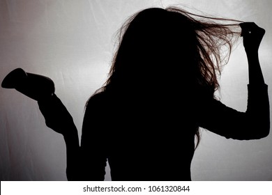 The Silhouette Of A Woman With Tangled, Dry And Damaged Hair With An Hair Dryer On A Dark Fabric Texture, A Concept Of Beauty And Health Care