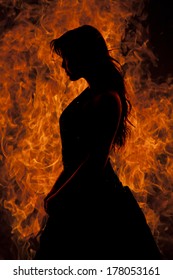 A silhouette of a woman that is standing in front of flames.