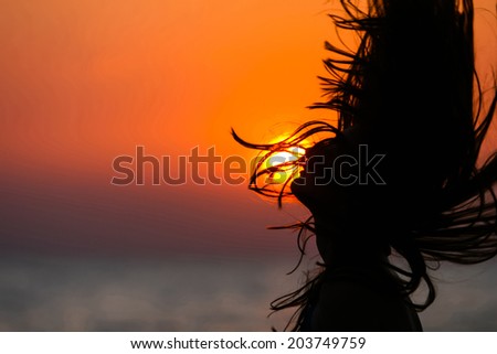 Silhouette of a woman tossing hair at sunset.