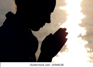 Silhouette of woman in  type, which sits ashore  and prays fold arms