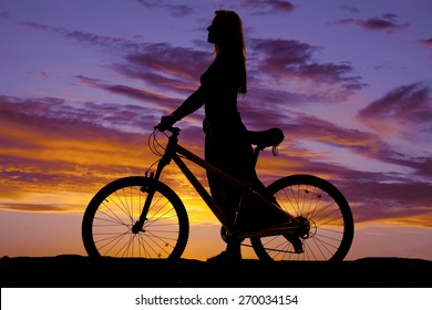 A silhouette of a woman walking with her bike.