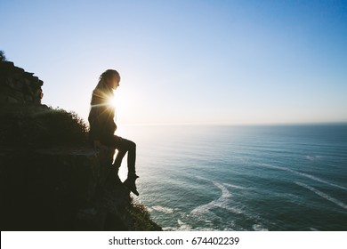 Silhouette of Woman wearing dreadlock sitting on cliff outdoor and looking to Atlantic Ocean - Powered by Shutterstock