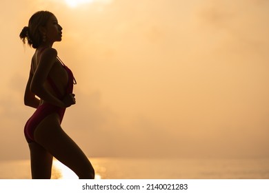 Silhouette : Woman Wearing Pink One Piece Swimsuit Enjoy Romantic Sunset Moment On The Stone, Tropical Beach.