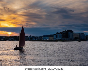 Silhouette of wooden sail boat going into harbor. Dark and dramatic sunset sky. Galway hooker wooden boat type. Galway city, Ireland. Water sport and hobby.