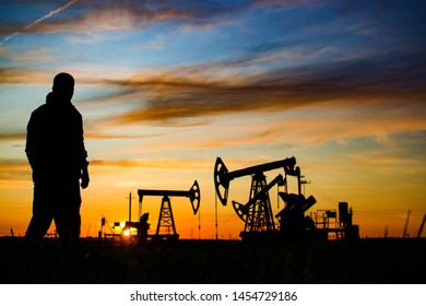 Silhouette of the worker on the background of oil rockers. Sunset. Oil production in Russia. exploration, oil and gas industry