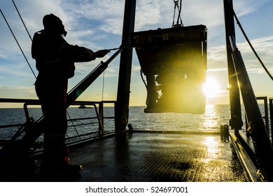 Silhouette of worker recovering robotics Remote Operated Vehicle (ROV) after entering sea surface during oil and gas pipeline inspection in the middle of South China Sea isolated on sunrise with glare