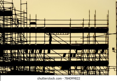 Silhouette Of Worker At Scaffolding, Working Day At Building Construction, Profile Structure Of Scaffolding Warm Colors Of Orange Sunset, Construction, Architecture And Engineering Work