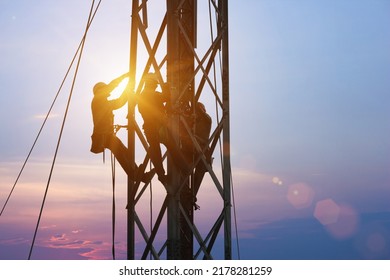 Silhouette Workers On Background Of Construction Crews To Work On High Ground Heavy Industry And Safety Concept. Construction Of The Extension Of High-voltage Towers On Blurred Sky Nature Background.