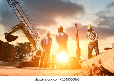 Silhouette Workforce engineers are looking at construction site blueprints through a blurry construction site at sunset.