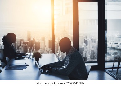 Silhouette, Working And Sitting In The City Office To Focus In The Morning. Business, People And Typing At The Boardroom Table At A Calm Time Of Day. Cityscape, Window And Flare View Of Urban Life.