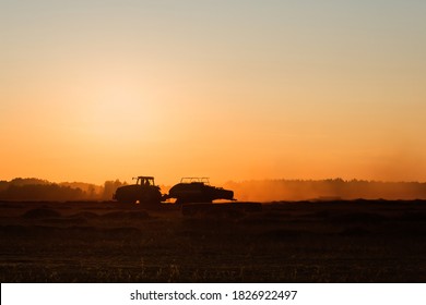 Silhouette of working tractor in autumn field in sunset time, tractor packing hay into rectangular bales, working machine in golden sky background, agriculture concept