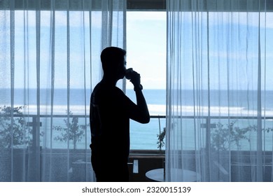 silhouette of young asian man drinking coffee in window with view of blue sea in luxury beach resort of bali.  Sunrise on vacation. - Powered by Shutterstock