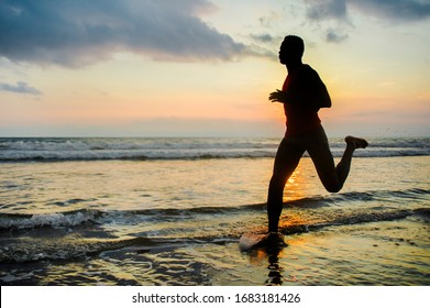 silhouette of young athletic and fit african american sport man doing running workout on sunset at the beach training hard jogging barefoot in healthy lifestyle concept - Powered by Shutterstock