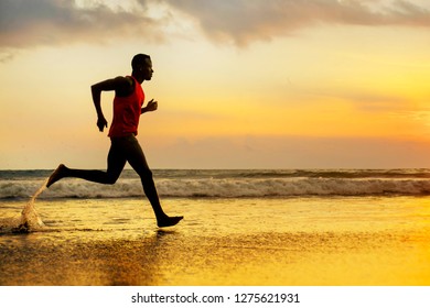silhouette of young attractive fit athletic and strong black African American man running at sunset beach training hard and sprinting on sea water in professional athlete and runner workout 