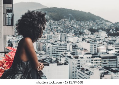 A silhouette of a young black slim woman with curly afro hair during lockdown or quarantine  observing a rainy urban landscape from a balcony of a high floor on a moody morning, Rio de Janeiro, Brazil