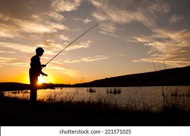 Silhouette Of A Young Boy Fly Fishing At Sunset