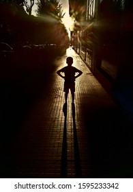Silhouette of a young boy with his hands on hips and in a fearless and confident superhero position, with the sun in the background