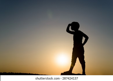 Silhouette of Young Boy Searching and Looking into the Distance with Hand Shielding Eyes, Backlit By Late Day Sun with Copy Space