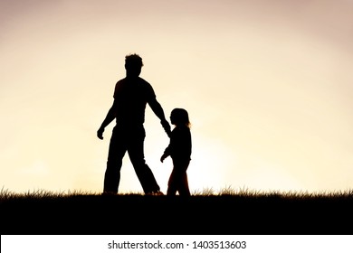 The silhouette of a young Christian father is guiding his young child by the hand as they walk outside at sunset.