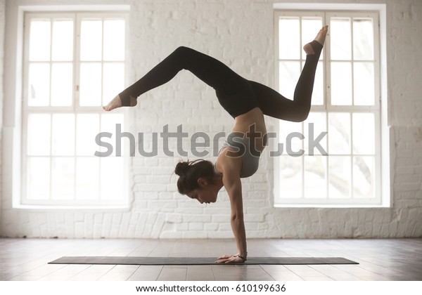 Silhouette of young cool attractive yogi woman\
practicing yoga concept, standing in Adho Mukha Vrksasana exercise,\
Downward facing Tree pose, working out, wearing sportswear bra and\
pants, full length