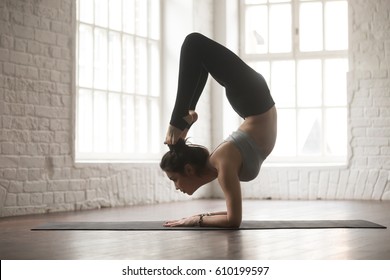 Silhouette of young cool yogi woman practicing yoga concept, stretching in vrischikasana exercise, Scorpion pose, working out, wearing black sportswear pants, full length, white loft studio background - Shutterstock ID 610199597