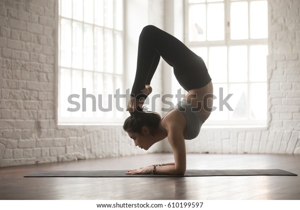 Silhouette of young cool yogi woman practicing\
yoga concept, stretching in vrischikasana exercise, Scorpion pose,\
working out, wearing black sportswear pants, full length, white\
loft studio\
background