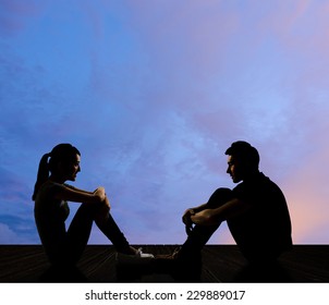 Silhouette of young couple face to face sit on ground in the city night.