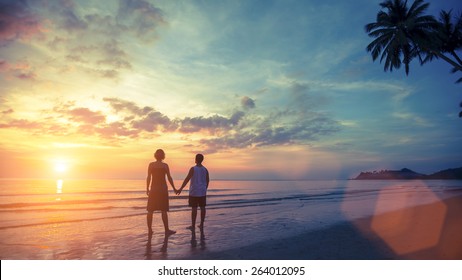 Silhouette of young couple on their honeymoon standing on Sea beach at amazing sunset.
