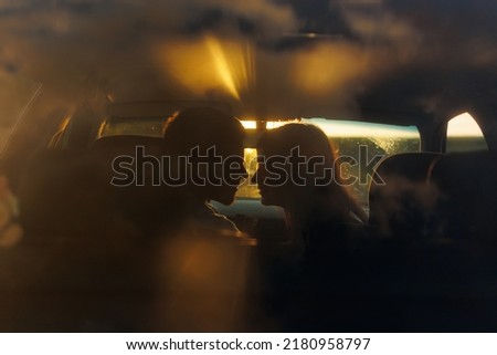 Silhouette of a young couple in the sunset light kissing in a car