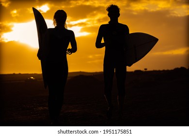 Silhouette Young Couple Surfers Stay On The Sunset Beach. Surfers Walking With Surfboards To The Beach. Extreme Sport, Travel And Vacation Concept.