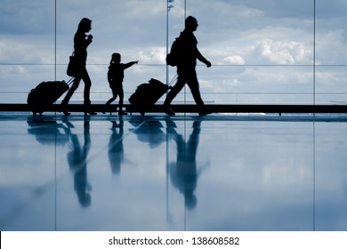 Silhouette Of Young Family With Luggage Walking At Airport, Girl Pointing At The Window