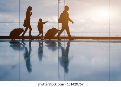 Silhouette of young family with luggage walking at airport, girl showing something through the window