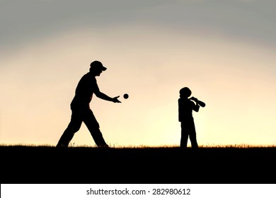 A silhouette of a young father and his little boy child playing baseball outside on a summer evening.