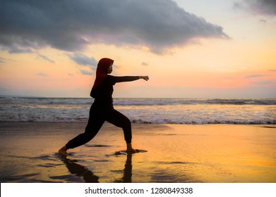 silhouette of young fit and aggressive Muslim woman covered in Islam hijab head scarf training martial arts karate punch attack and fitness workout at beautiful beach sunset in defense concept - Powered by Shutterstock