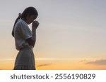 Silhouette young girl with hands folded praying worship at sunset. worship god with christian concept religion.