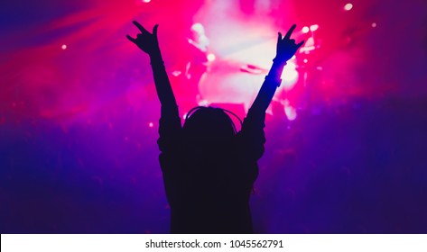 Silhouette Of Young Girl Partying On Concert In Nightclub.Music Hall Background.Young Woman Put Hands Up To Music With Rock On Gesture.Rock & Roll Concert Audience Backdrop.Female Wave Hands In Club 