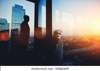 Silhouette of young intelligent man managing director resting after late business meeting while standing near big office window background with copy space for your text message or promotional content - Shutterstock ID 330863699