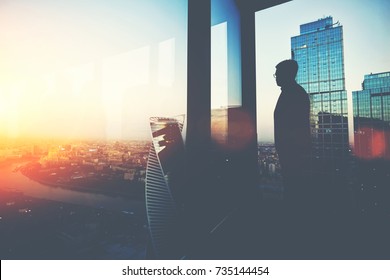 Silhouette of young intelligent man managing director resting after late business meeting while standing near big office window background with copy space for your text message or promotional content
